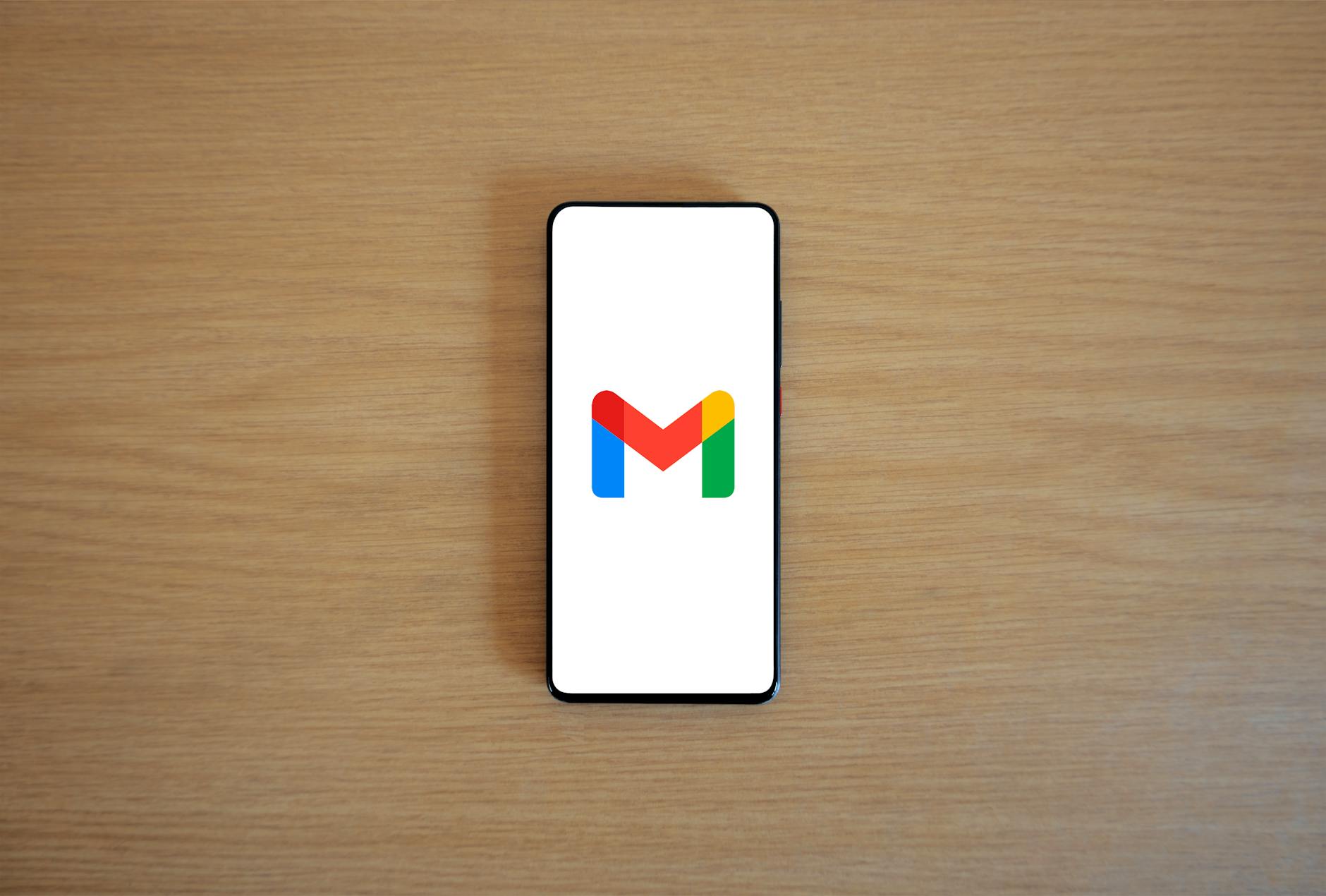 A smartphone displaying the Gmail app logo on a wooden surface, viewed from above.